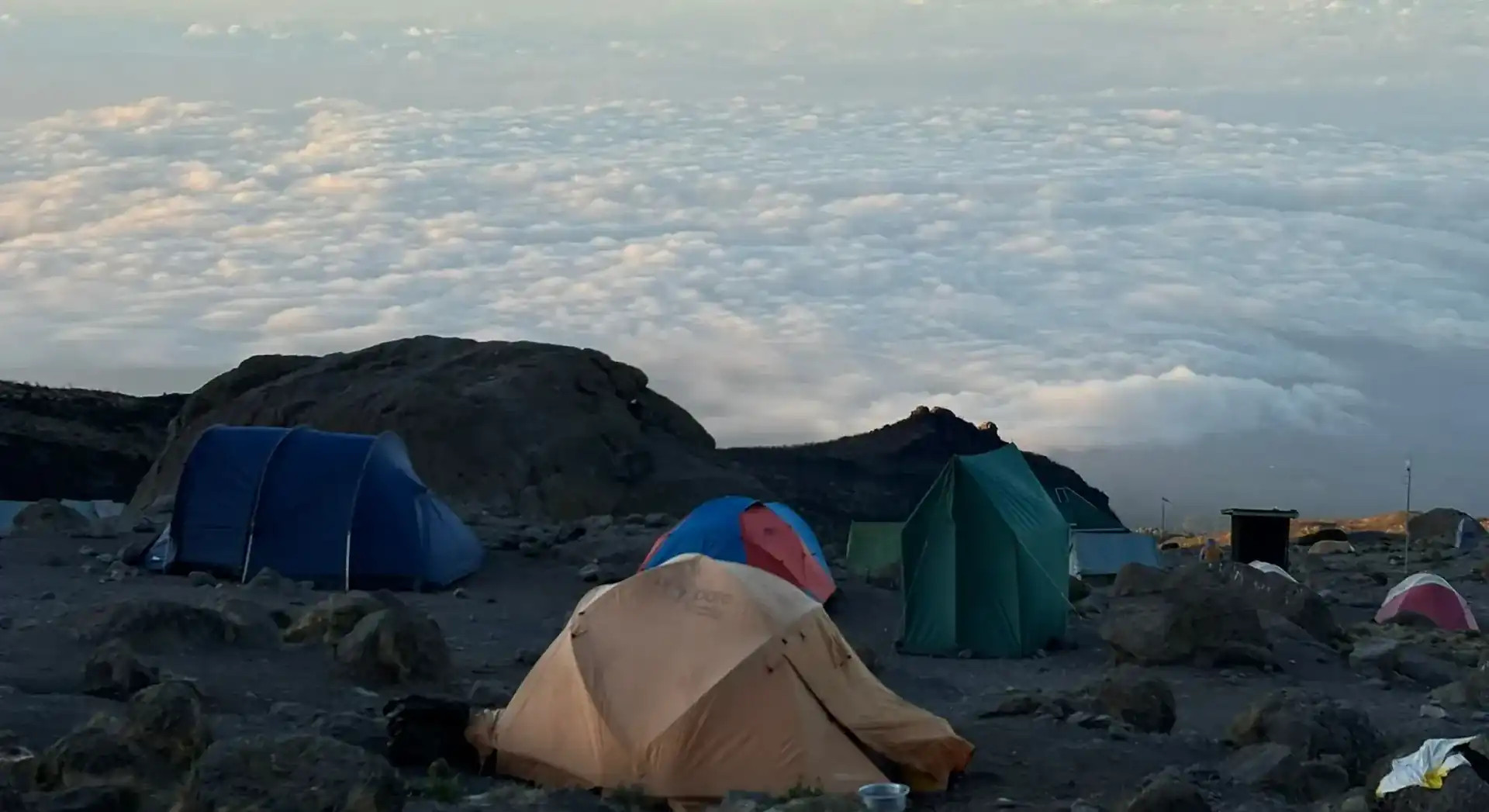 Ascend Tanzania high-altitude yellow expedition tent glowing at sunset above sea of clouds