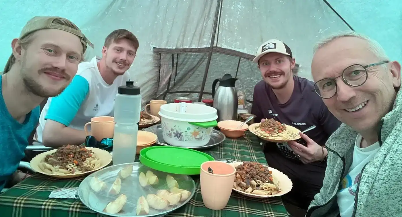 Expedition dining table with mountain meals, soup, and fresh fruits inside mess tent
